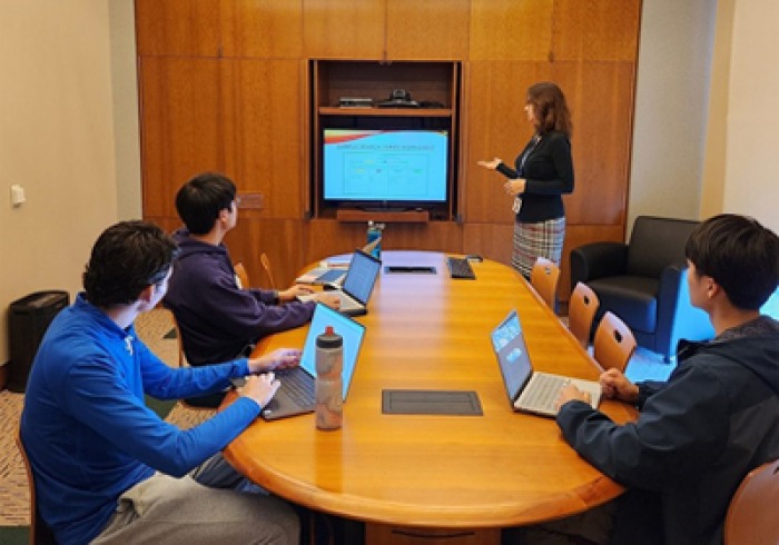 Librarian Jenn Tirrell leads a workshop in the Library with students sitting at a round table, looking at a screen.