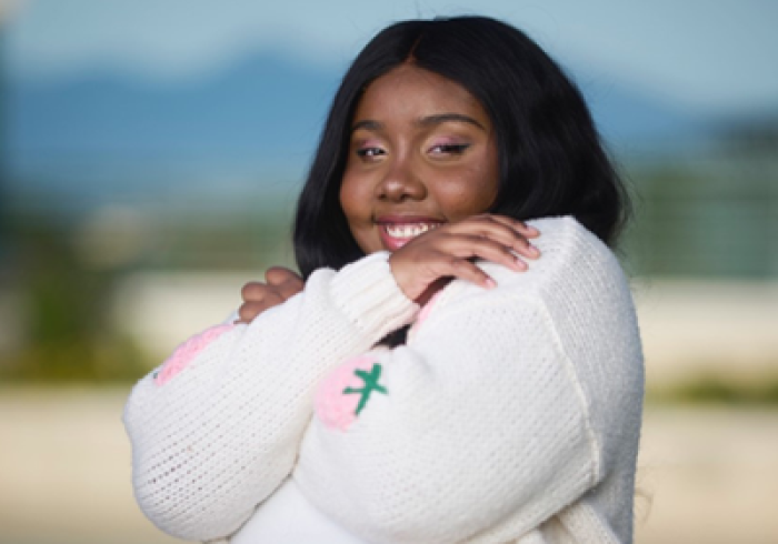 Sasha Woods smiles and hugs herself as she poses outside on Soka's Campus