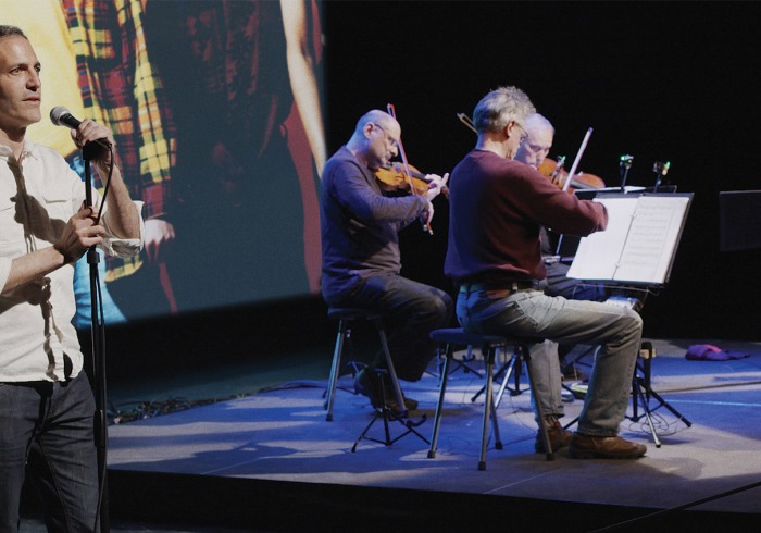 Man at microphone and four musicians sitting playing