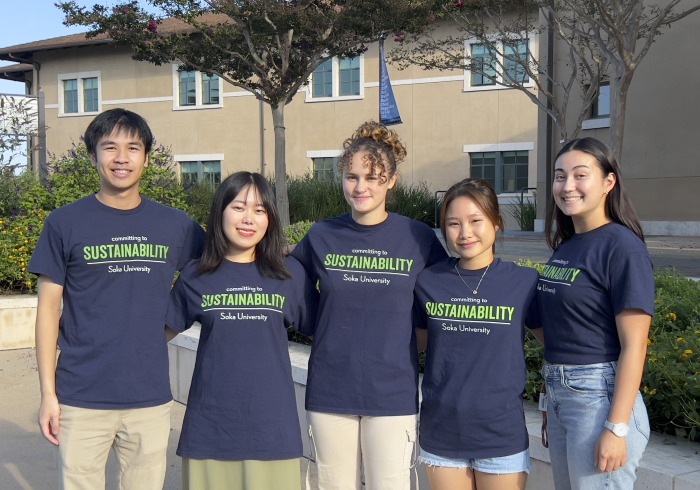 A picture with 5 students standing shoulder to shoulder, smiling at the camera