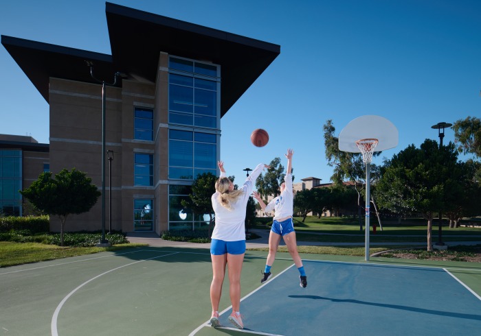 2 students playing basketball at the basketball court within the residential area.