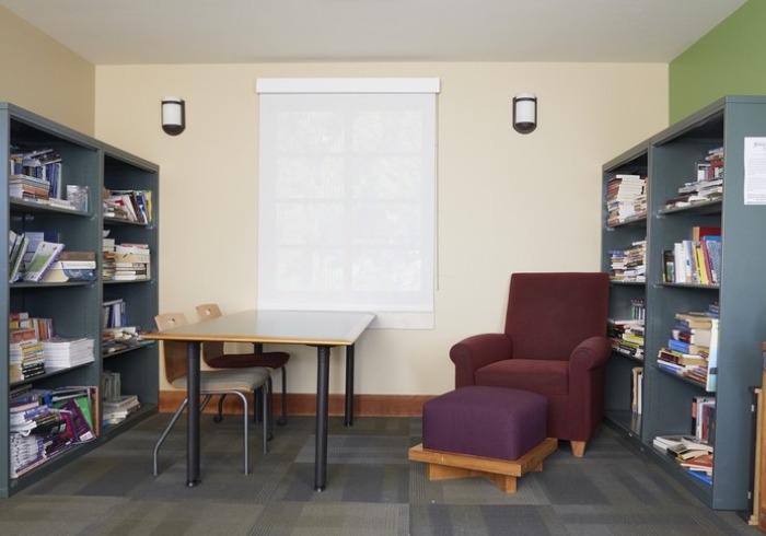 a room with 2 bookshelves on opposing sides of the room with a table and maroon sofa chair in the middle.