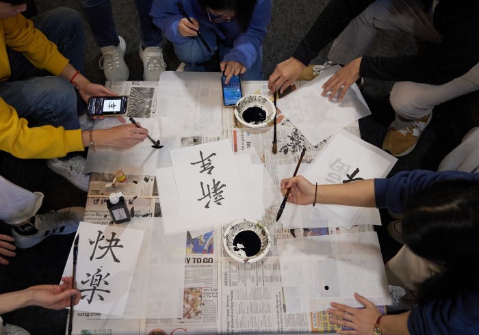 Overhead shot of students gathered around a table practicing Chinese calligraphy.
