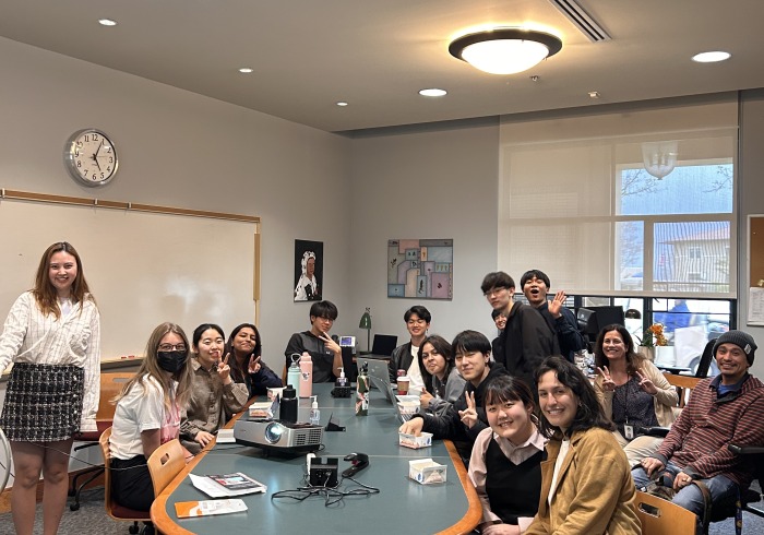 Many students are gathered around a large table smiling at the camera.