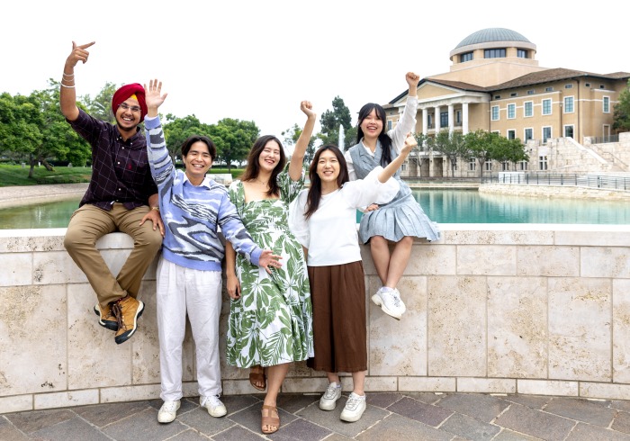 Five undergraduate students smiling in front of Peace Lake and Founders Hall at Soka University of America