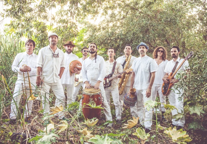 JUNGLE FIRE bandmembers wear all white outfits with various hats and hold their instruments in a wooded area.
