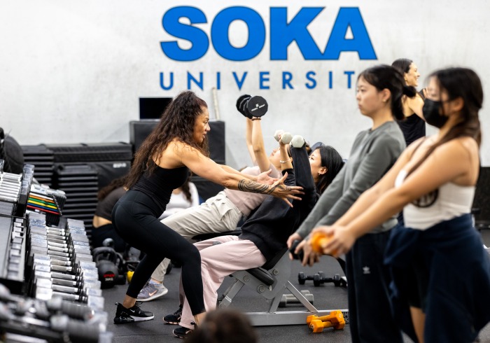 A fitness instructor helps students lift weights during a class.