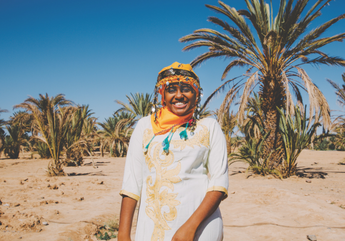 A woman smiles while wearing traditional garb in a desert. 