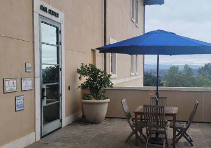 Exterior of Mail Center with mail slots, posted hours, and a picnic table with blue umbrella outside the entrance.