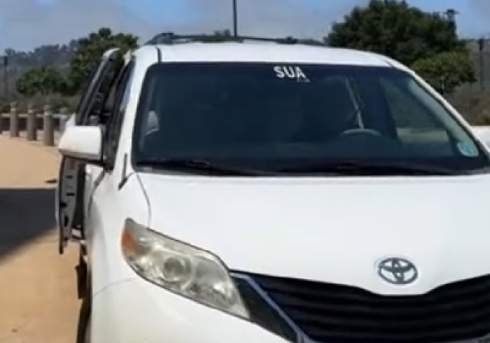 White mini van with SUA written in top center of windshield waits with its door open on SUA's campus.