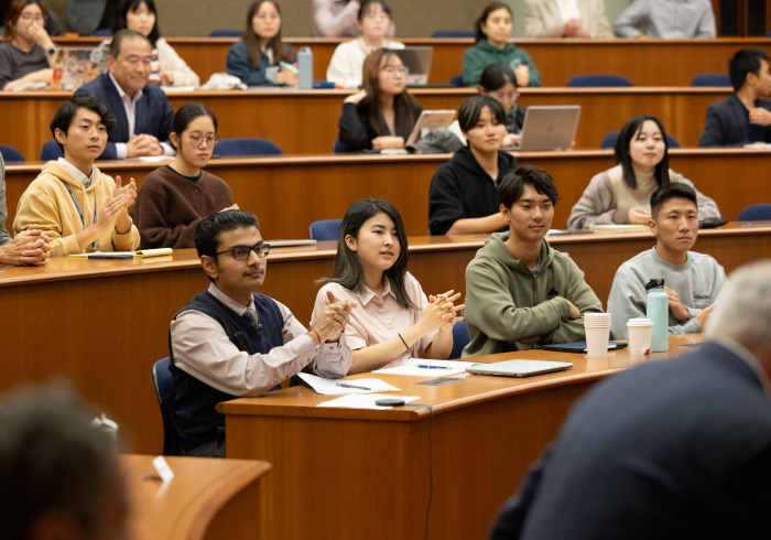 A diverse group of students and staff applaud a speaker during a presentation in an auditorium.