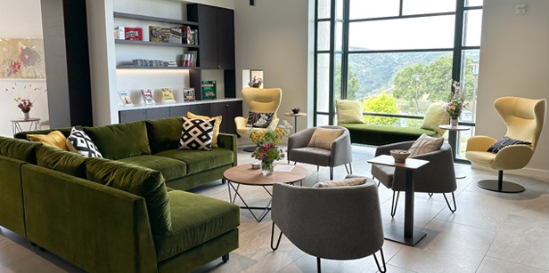 Interior shot of new Global Language and Culture Center featuring gray and green chairs, a velvet green couch, a bookcase with magazines, and a kitchen