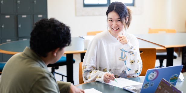 A girl is smiling and discussing her paper with a professor