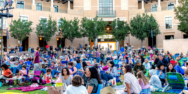 Summer at Soka attendees sit on lawn chairs and blankets on the Campus Green in front of Ikeda Library.