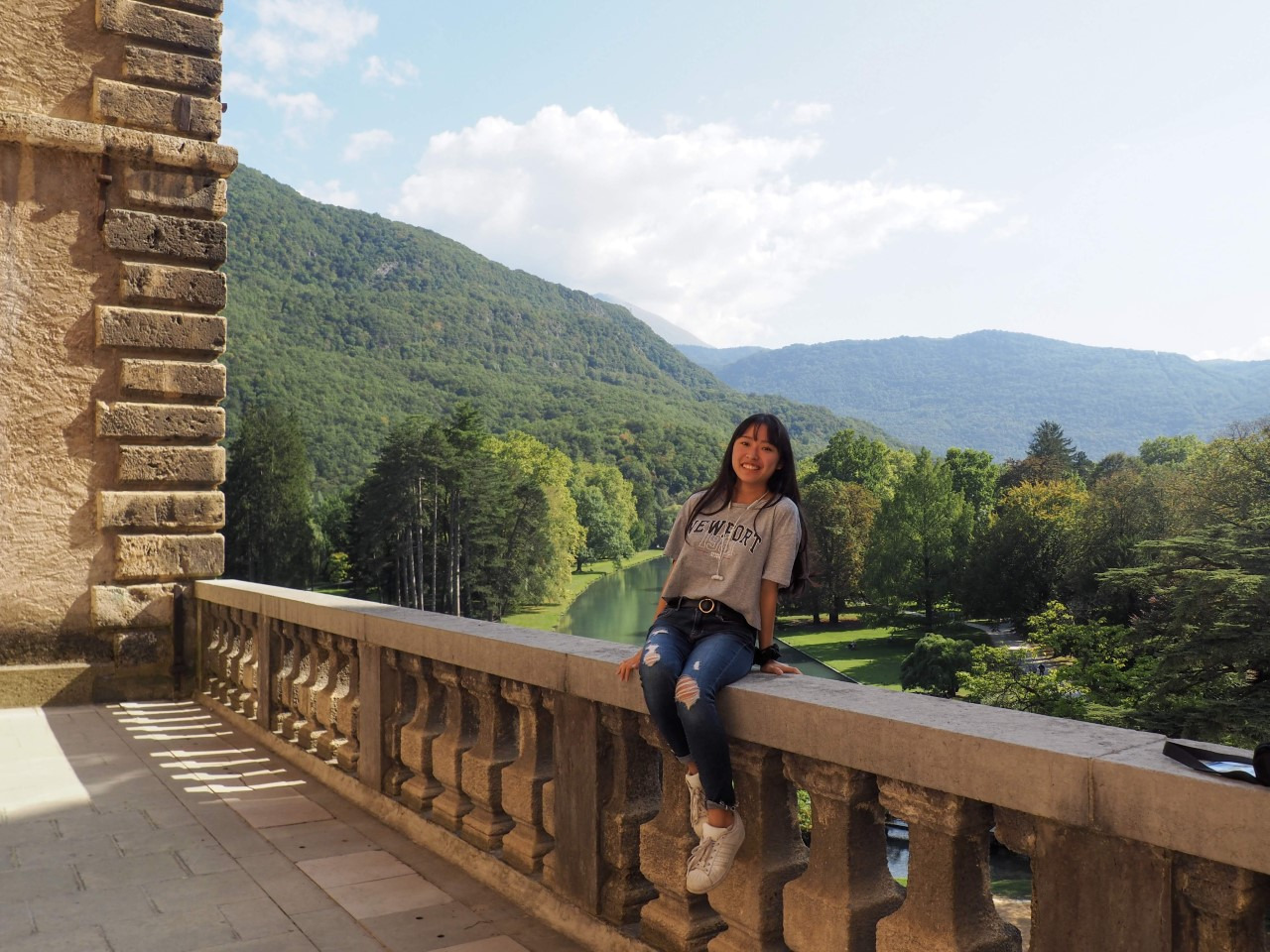 student sitting on ledge with green hills in background