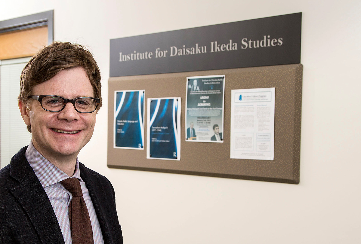 Jason Goulah stands in front of Institute for Daisaku Ikeda Studies bulletin board