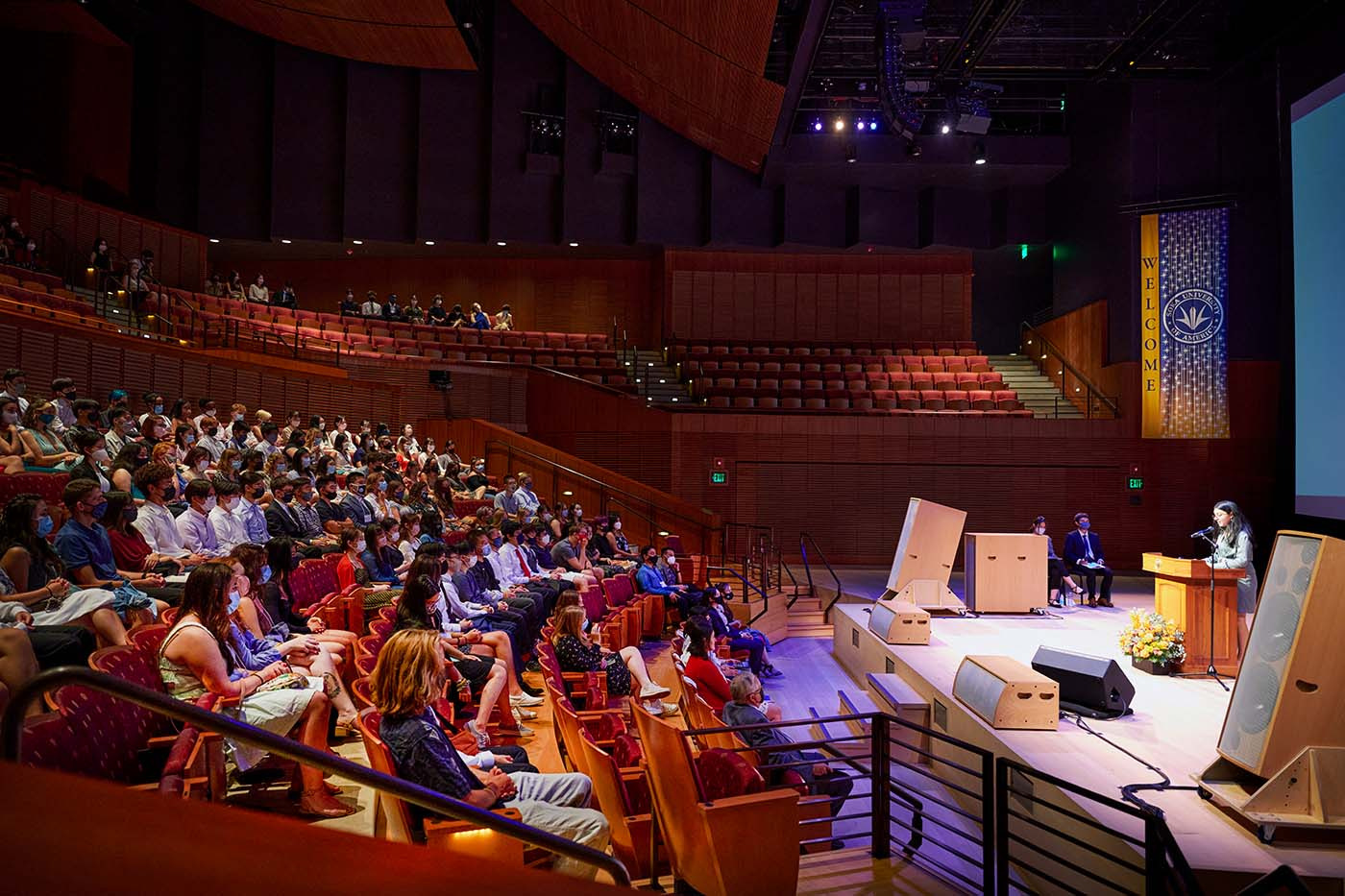 Person on concert hall stage speaks to students in audience