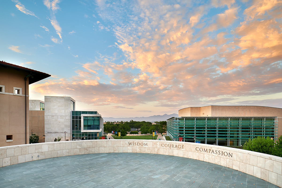 Central values of Soka University, Wisdom, Courage, and Compassion displayed on a wall in front of clouds and silhouetted mountains in the background