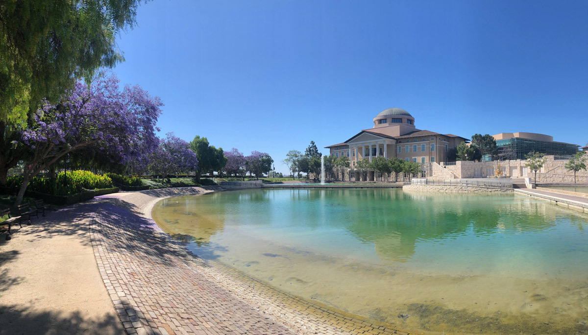 A photo of Founders Hall taken across Peace Lake surrounded by flowering purple trees