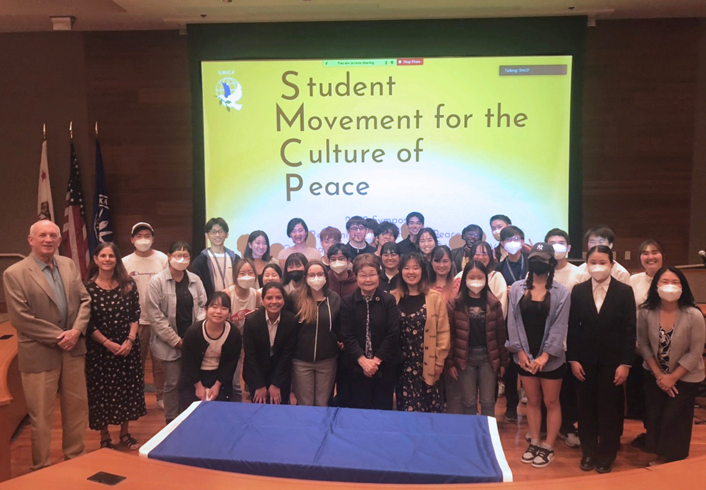 Students and Faculty pose in front of a projected screen that reads "Student Movement for the Culture of Peace"