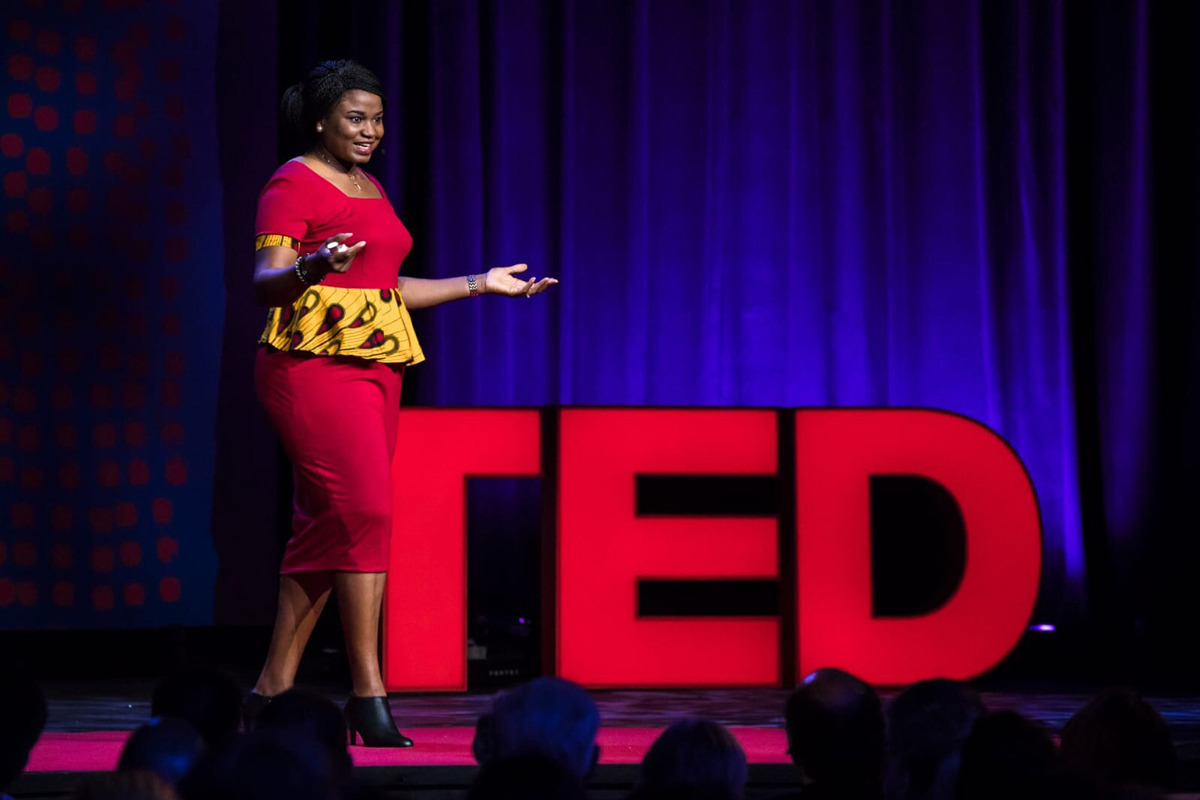 Professor Chika Esiobu stands in front of big red letters spelling out TED as she speaks on stage during her TED Talk