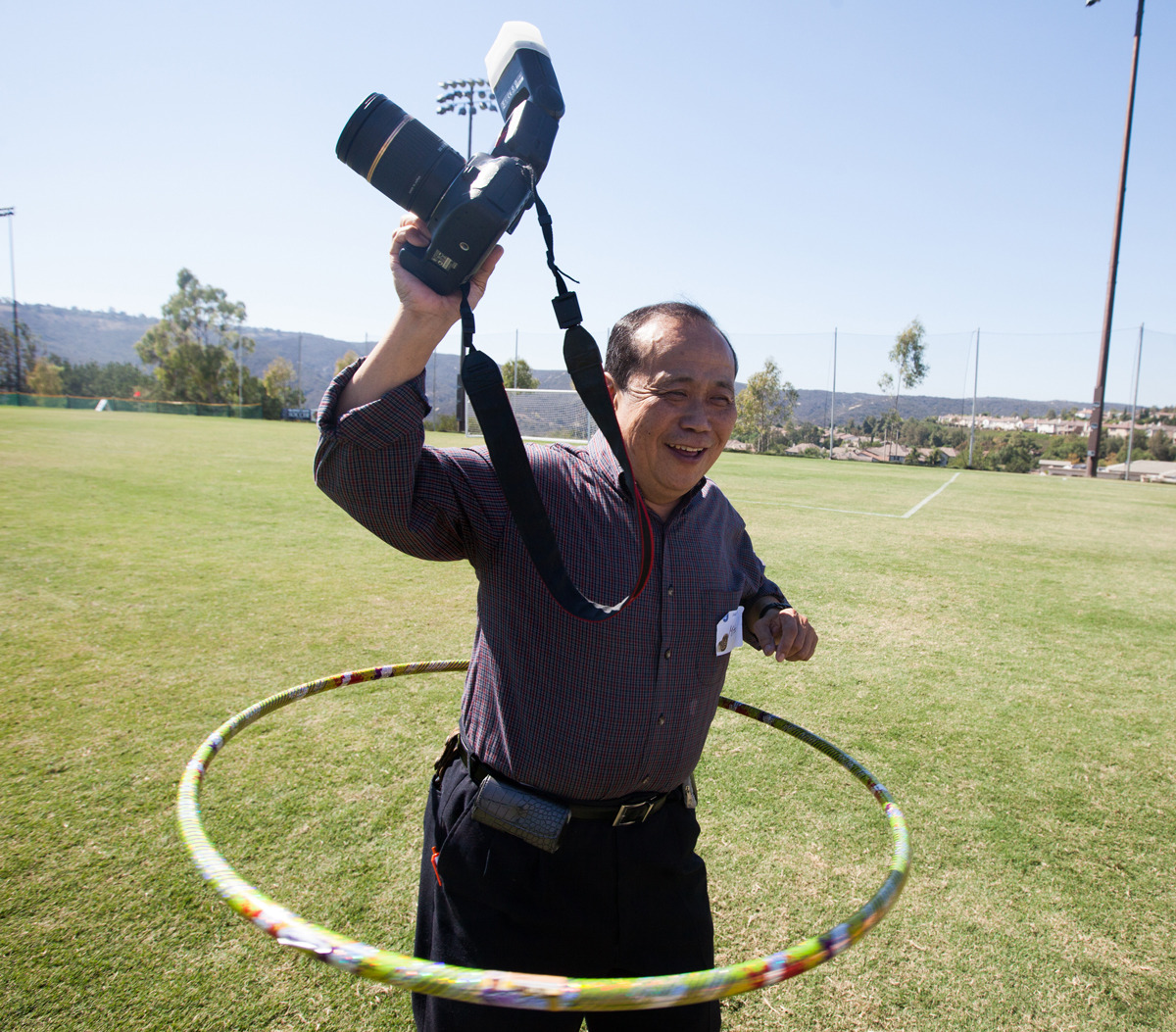 Mitsu Kimura smiles and holds his camera up as he is hula hooping