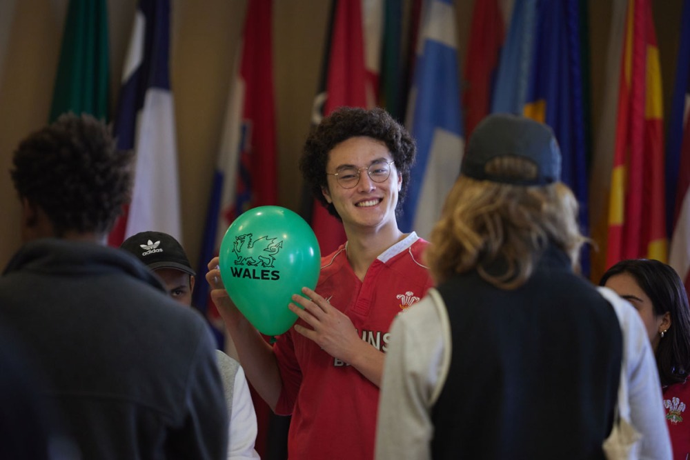 A student smiles as he holds a green balloon that displays a dragon and the word "Wales"