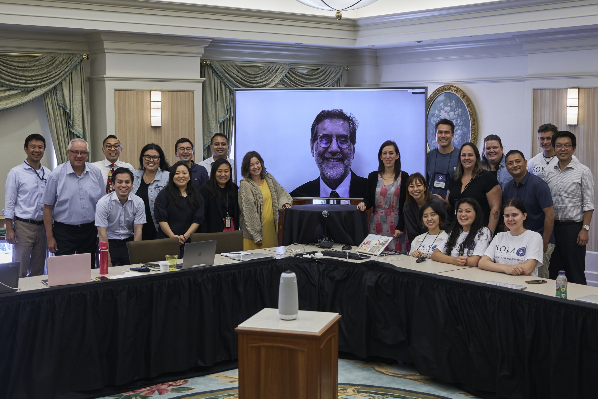 Members of SIGS pose for a photo in front of a tv screen featuring Andrea Bartoli, Executive Adviser of SIGS