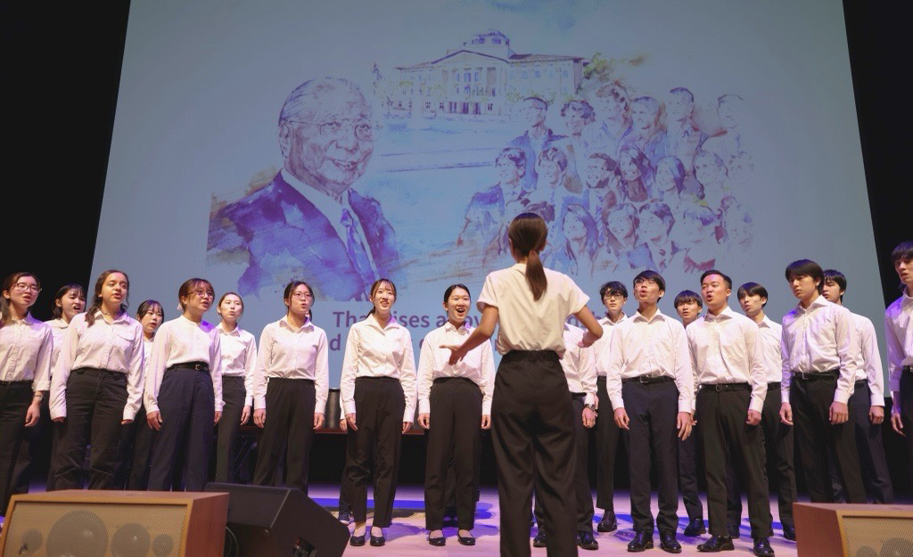 SUA student chorus signs the Light of Hope in front of drawing of Daisaku Ikeda 