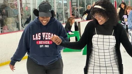Two students hold hands and smile as they ice skate.