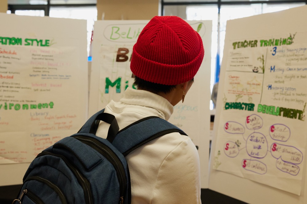 A student wearing a red beanie and blue backpack looks at a presentation.