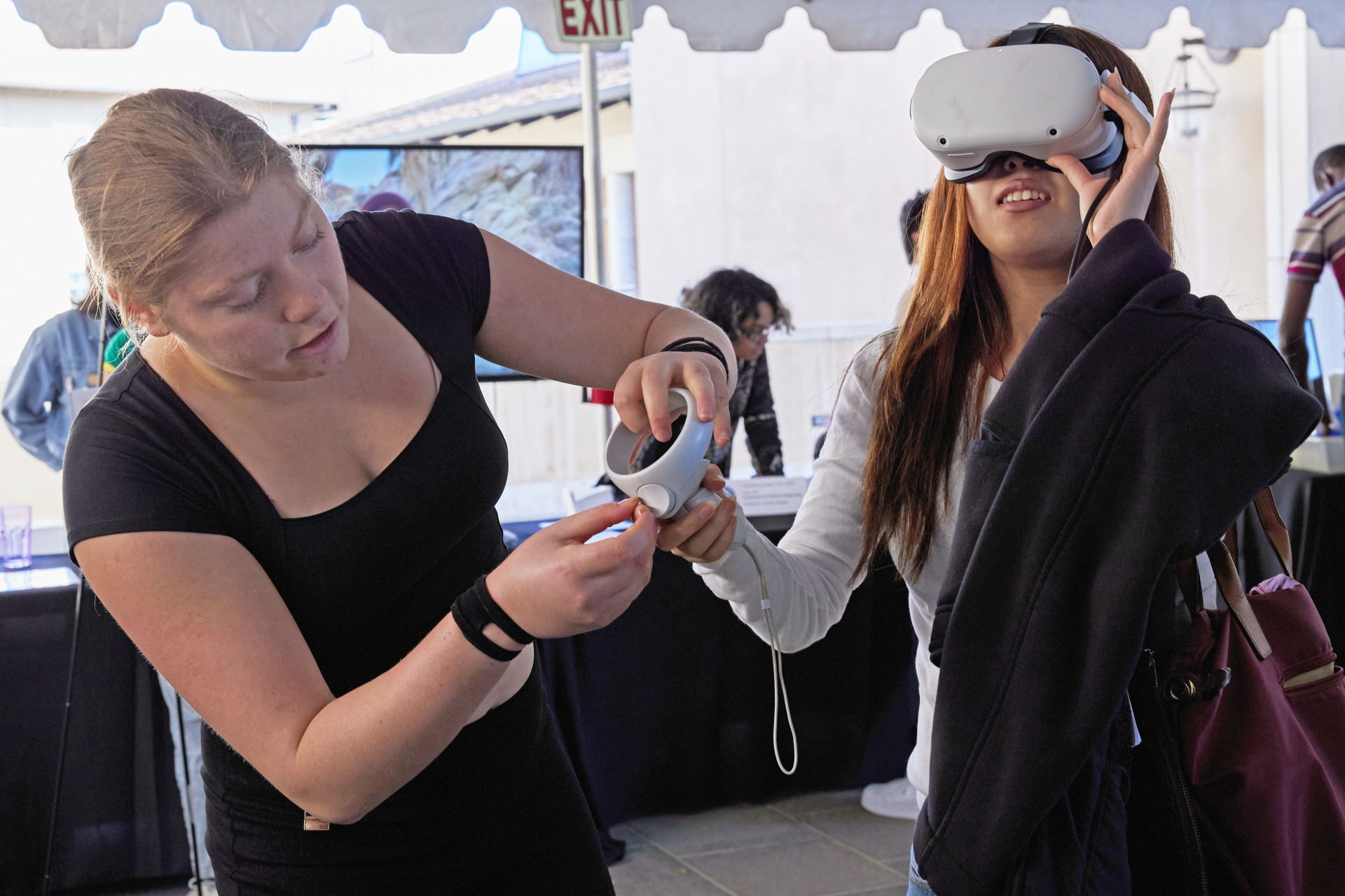 A woman wearing a VR headset is assisted by another woman.