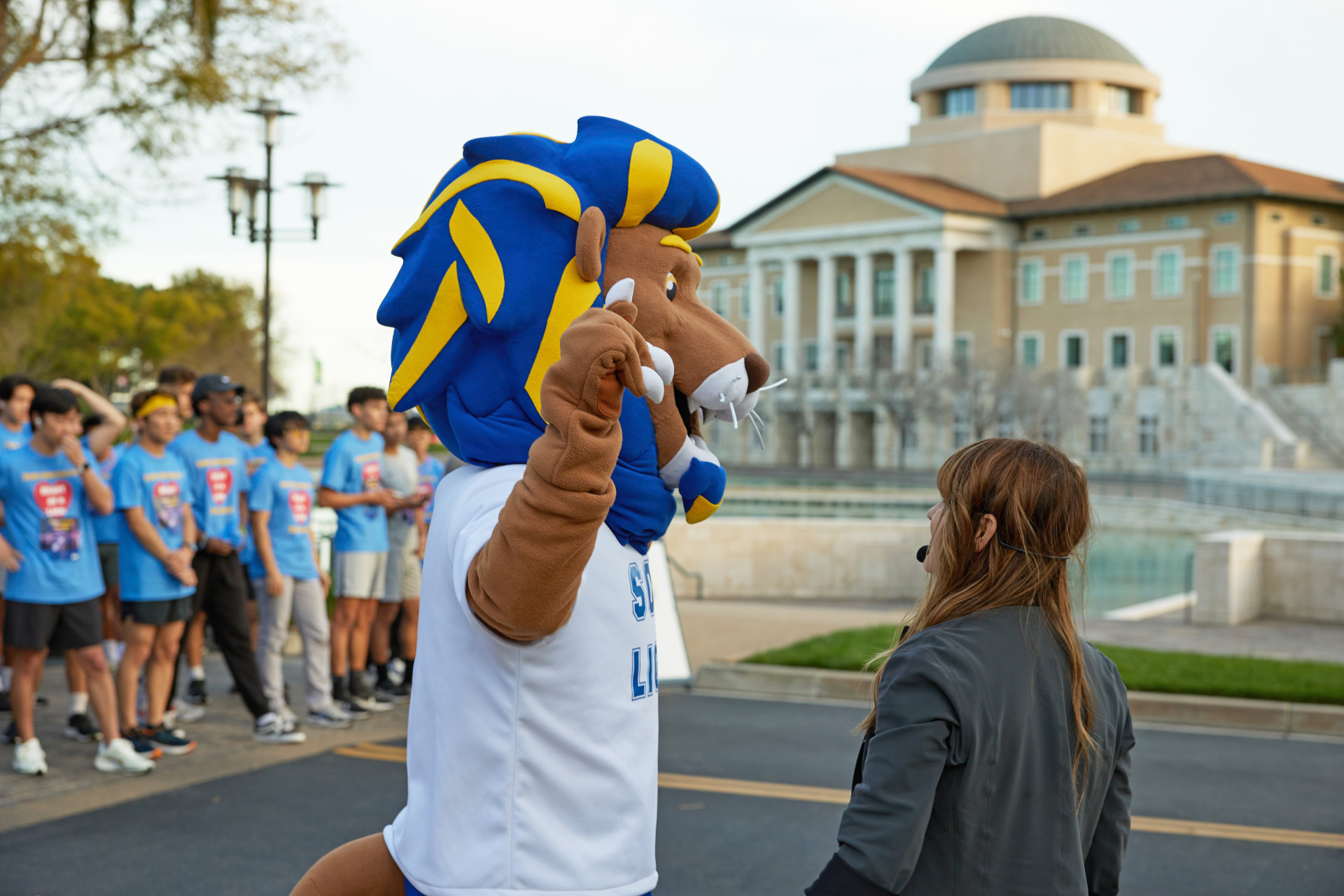 Leo the Lion speaks with Erica Baldaray in front of Founders Hall and Peace Lake before the start of the Heart of a Lion 5k.