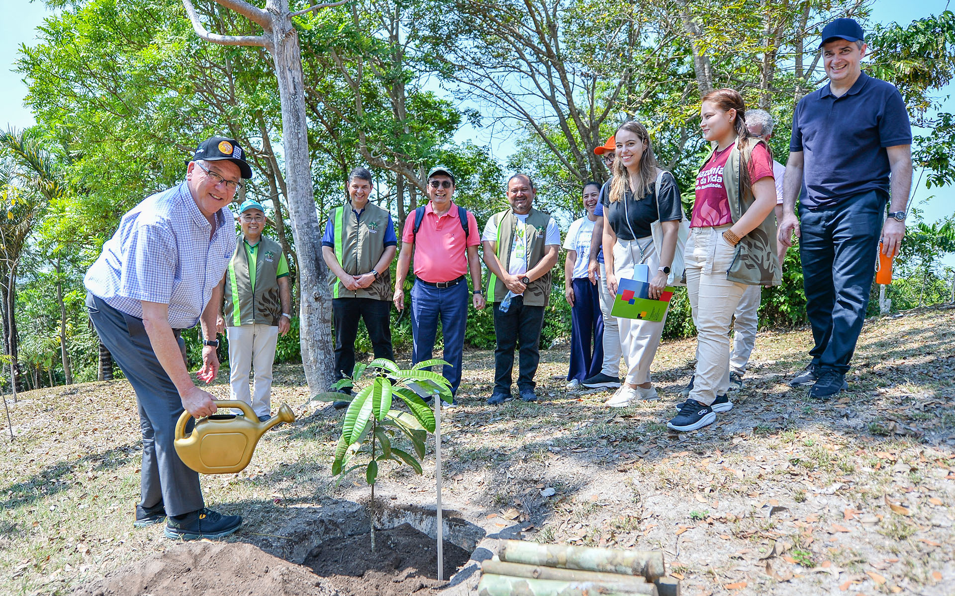 SUA President Ed Feasel waters a plant at the Soka Amazon Institute while a group of people look on