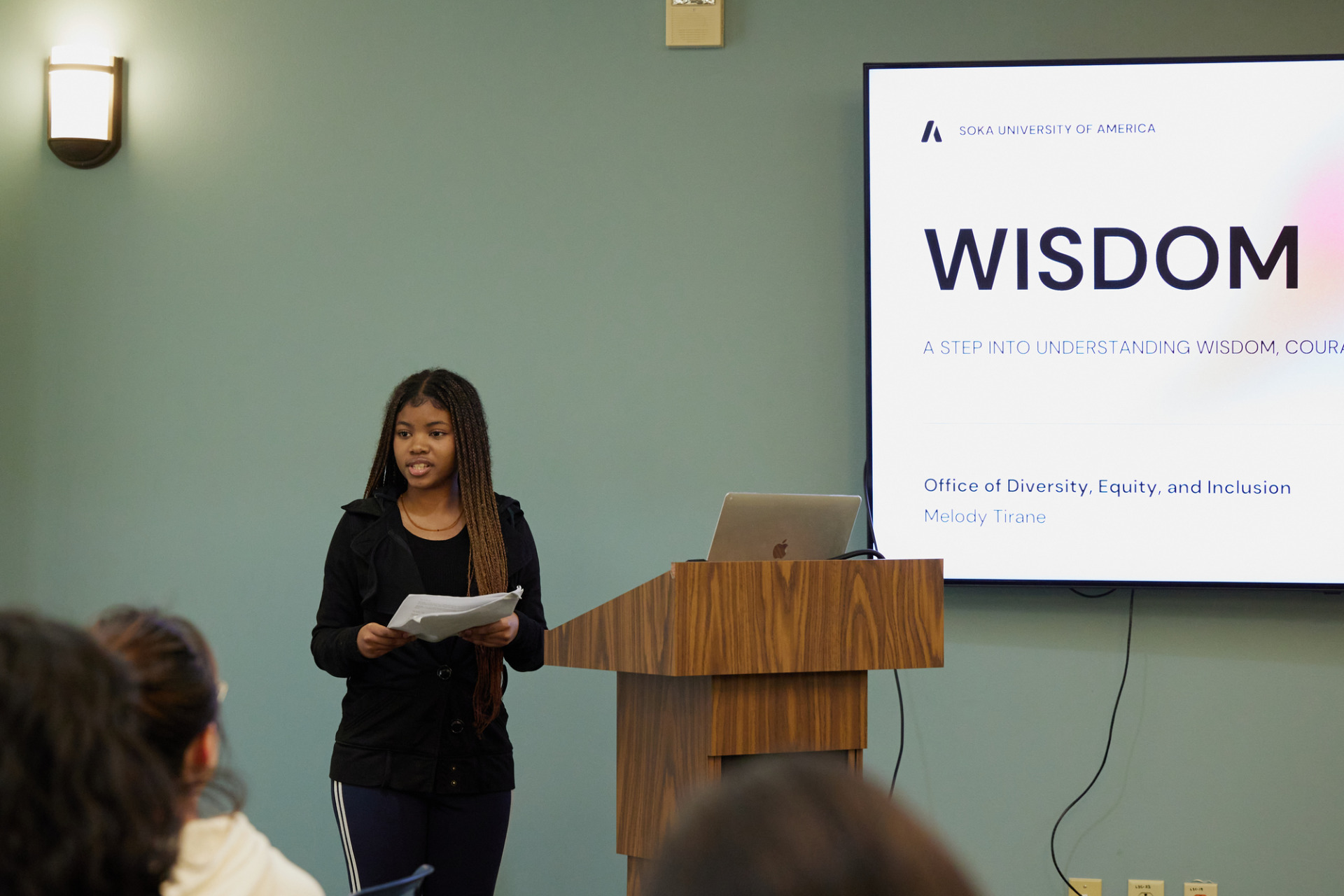 A speaker stands beside the podium as she presents during a seminar series