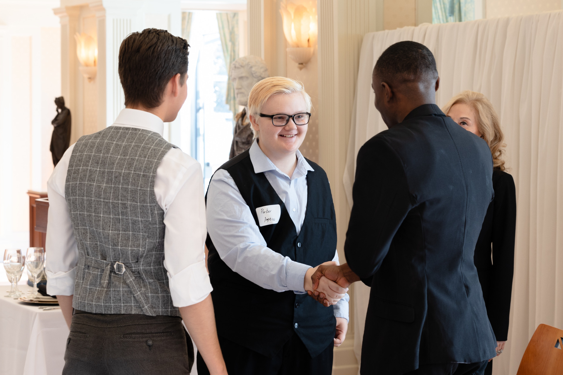 People dressed in business attire shake hands at an etiquette training event.