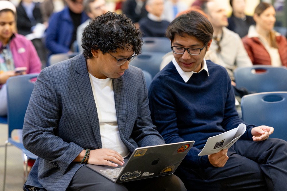 Two students look at documents and a laptop during the conference.