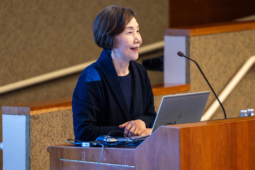 A woman smiles at the audience as she stands in front of a lectern while giving a presentation.