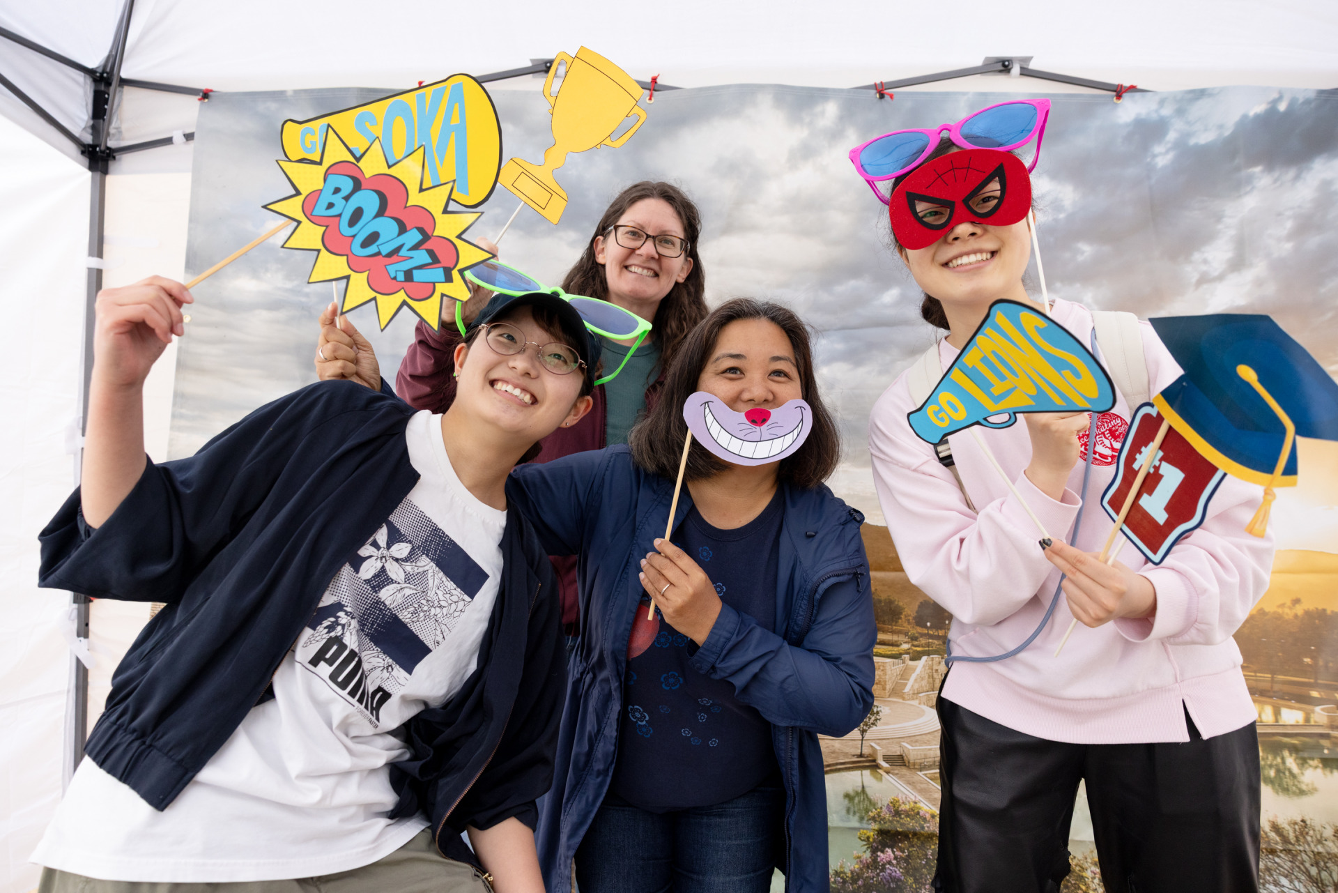 Four people pose with props in front of an SUA campus backdrop during the 2025 Soka Homecoming event.