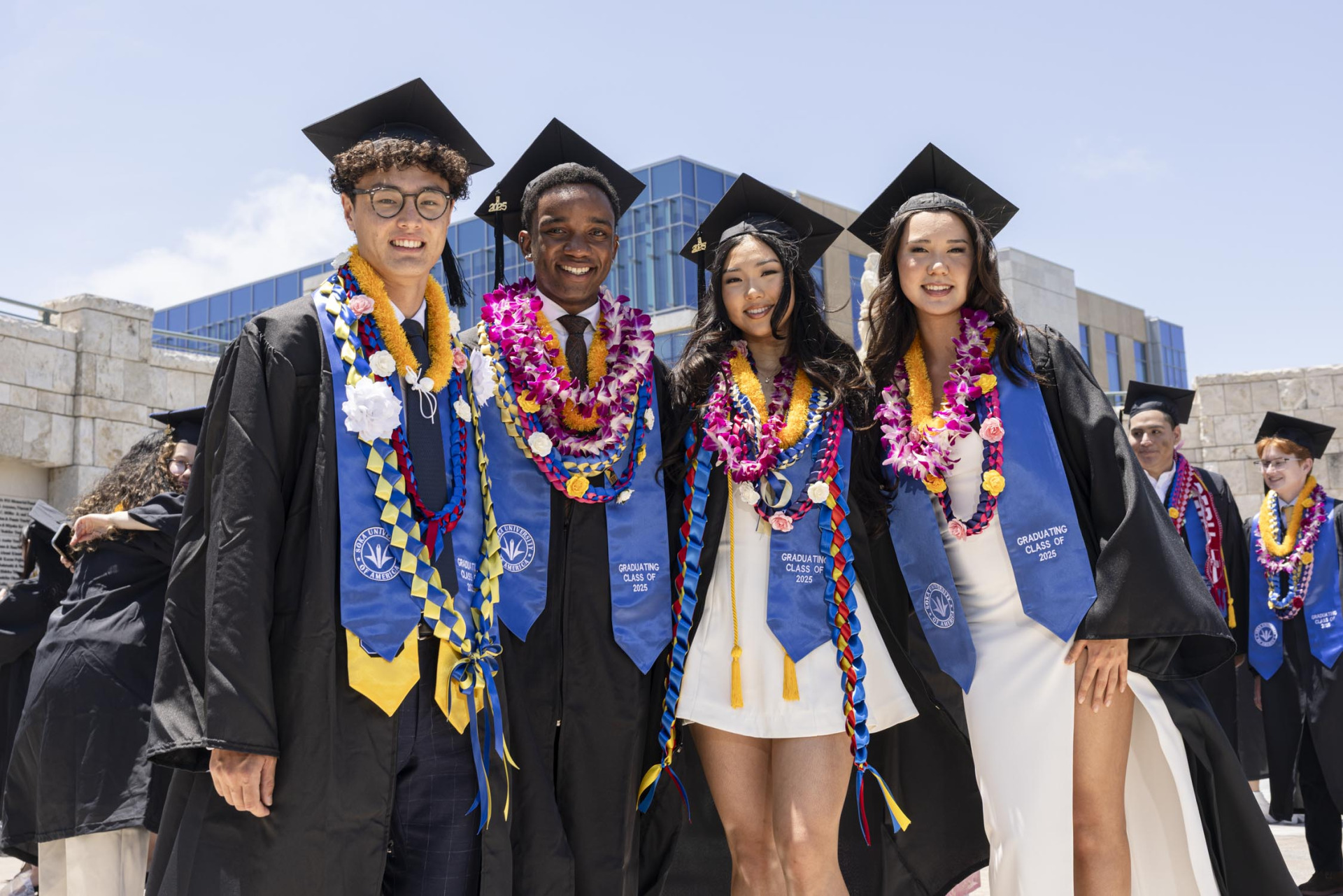 Four members of SUA's Class of 2025 smile in their cap and gown during commencement day.