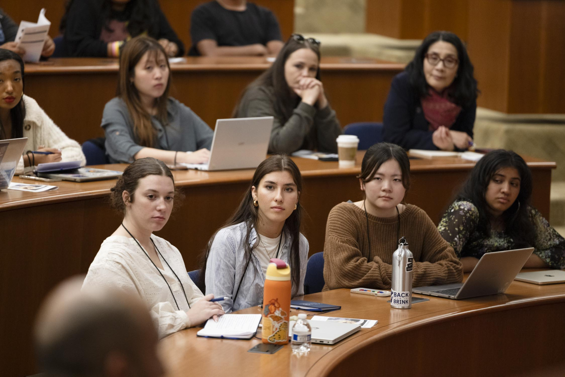 Four students sit alongside eachother at a wooden desk and listen intently to a speaker during the Nuclear Politics 2025 summer program.