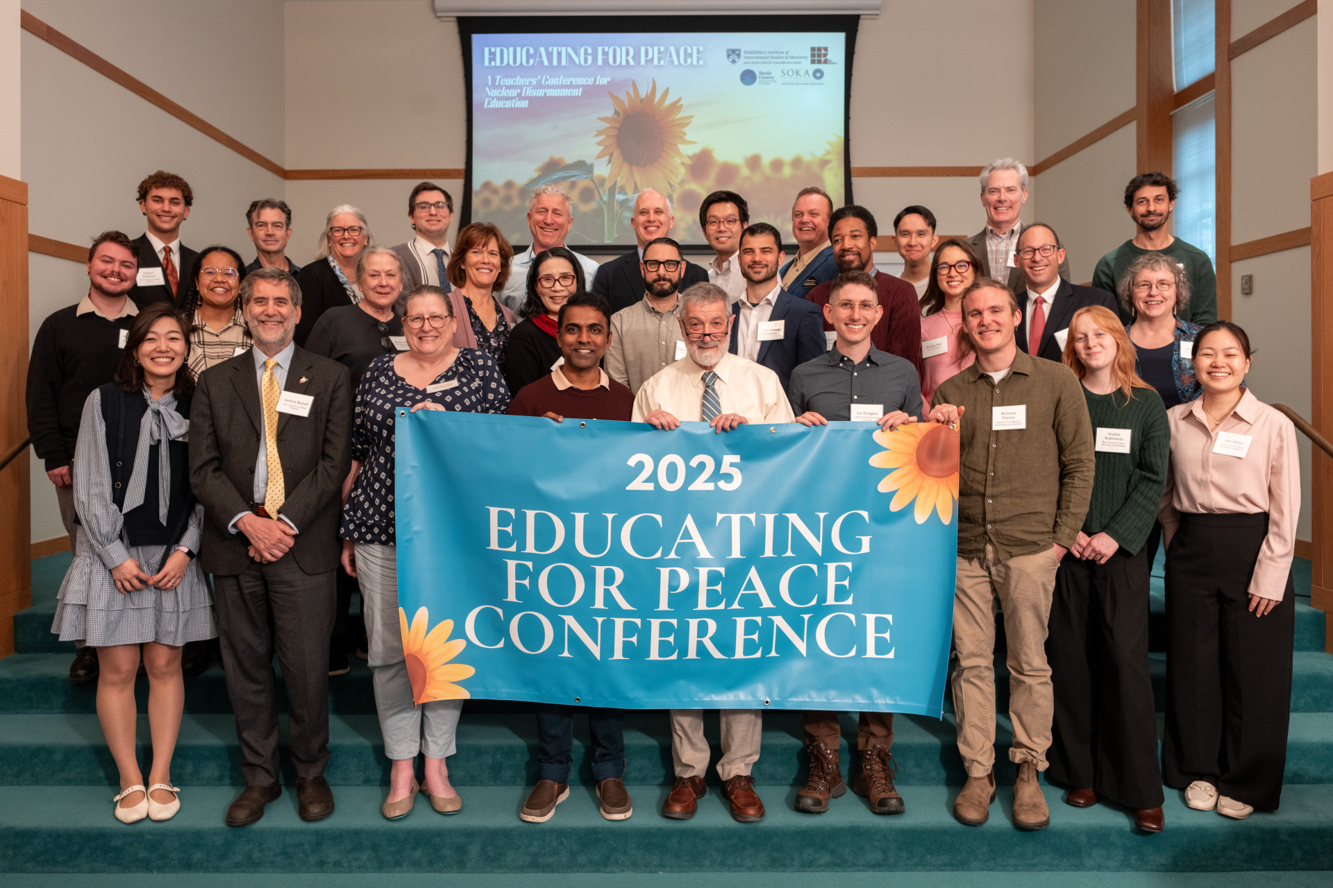 Participants of "Educating for Peace: A Teachers’ Conference for Nuclear Disarmament Education" gather for a group photo holding up a banner stating "Educating for Peace Conference"