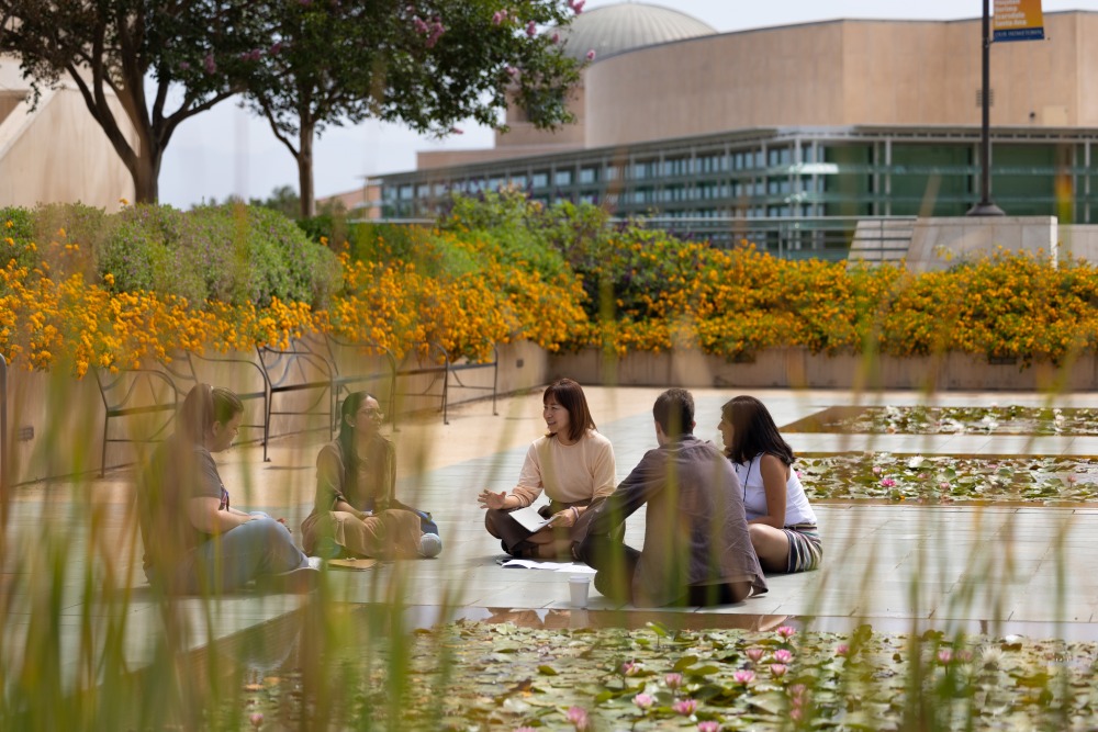 Five people sit on the ground in a circle by the lily ponds on SUA's campus.