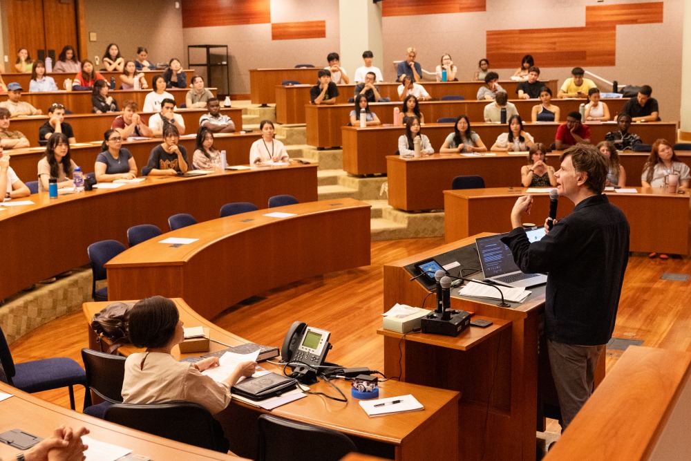 Jason Goulah, distinguished visiting professor of Ikeda Studies, speaks into a microphone in an auditorium full of students.