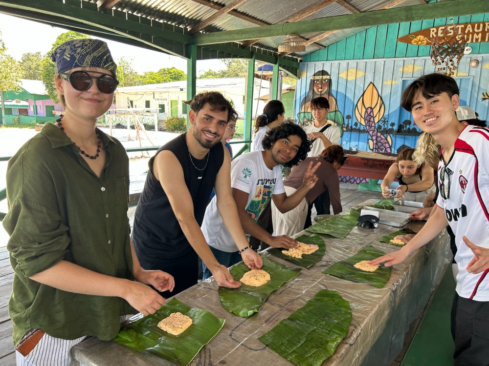 Students prepare food on top of large green leaves during a culinary workshop.