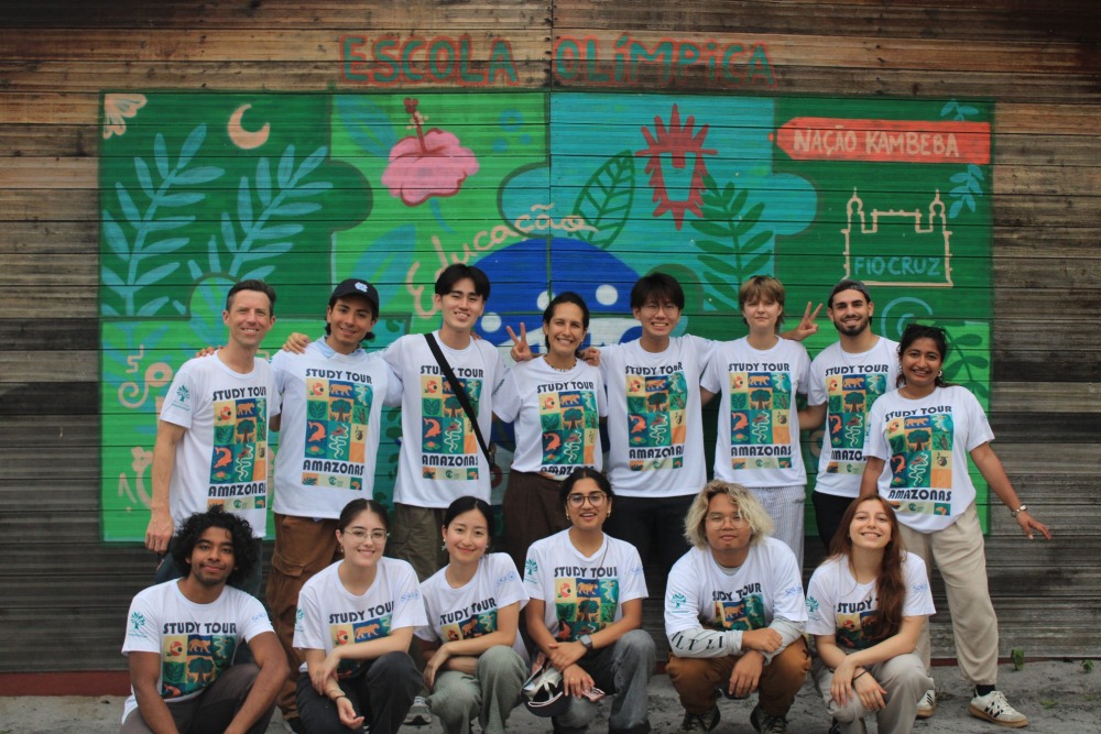 Students wearing matching white "Study Tour" t-shirts pose for a group photo in front of a mural.