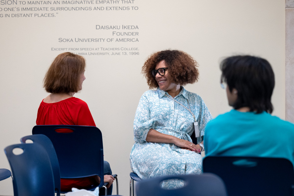 A woman with black glasses and short curly brown hair is smiling while talking with another woman in red dress