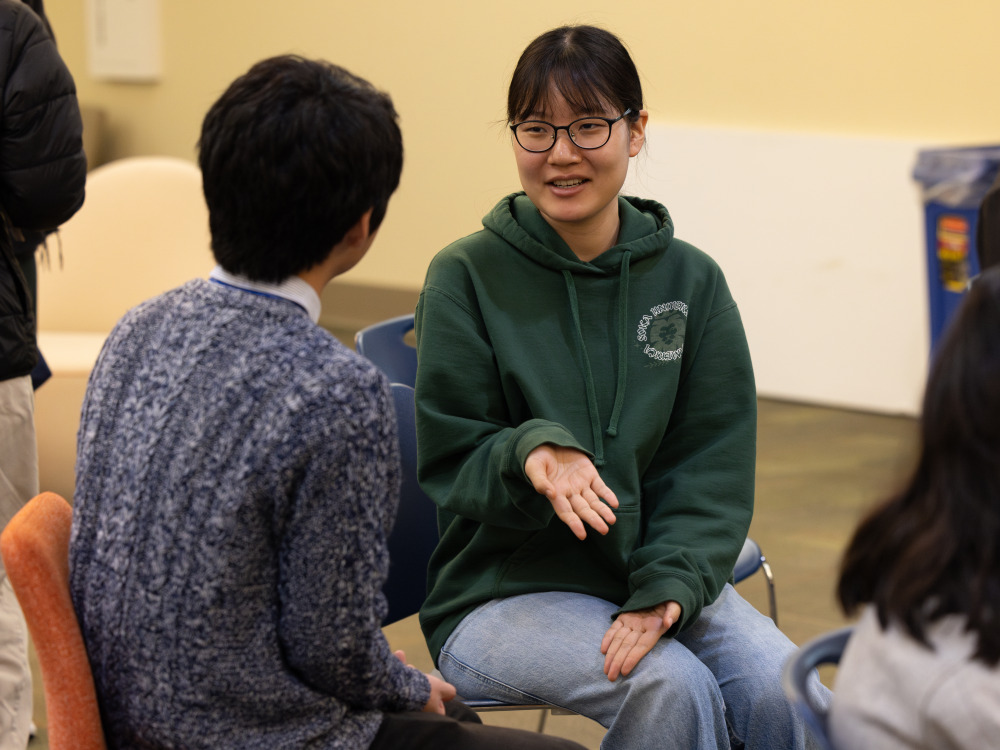 A female student in a green hoodie talks to a man in gray sweater 