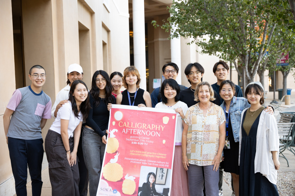 A group of students and faculty standing together, smiling and taking photos with the banner of the calligraphy event
