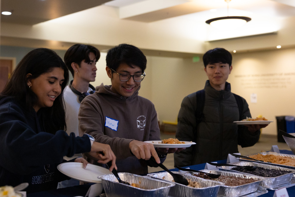 Some students smilling, standing in a line to take food for lunch